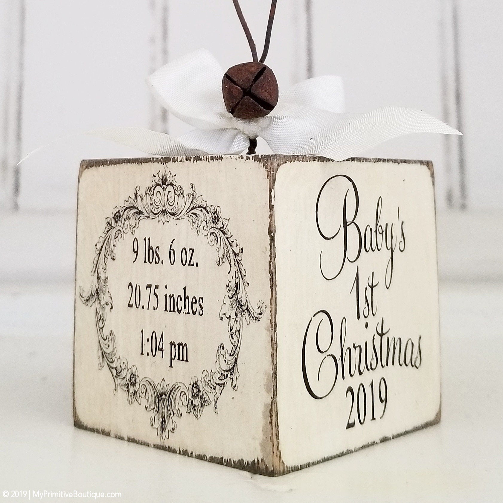 Decorative wooden block with 'Baby's First Christmas' text and decorative elements on a distressed background.