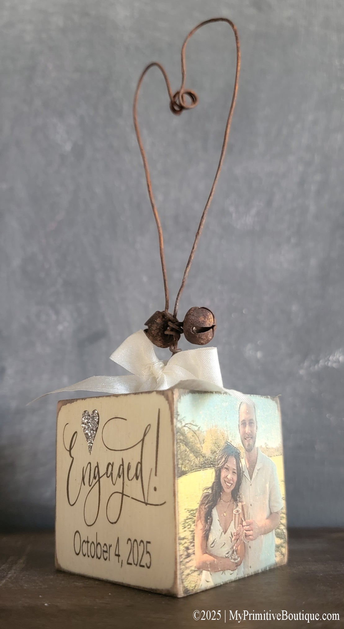 Personalized engagement photo ornament with rustic wire heart, ivory bow, glitter heart accent, and engraved text “Engaged! October 4, 2025.” Features custom couple photo on the side.