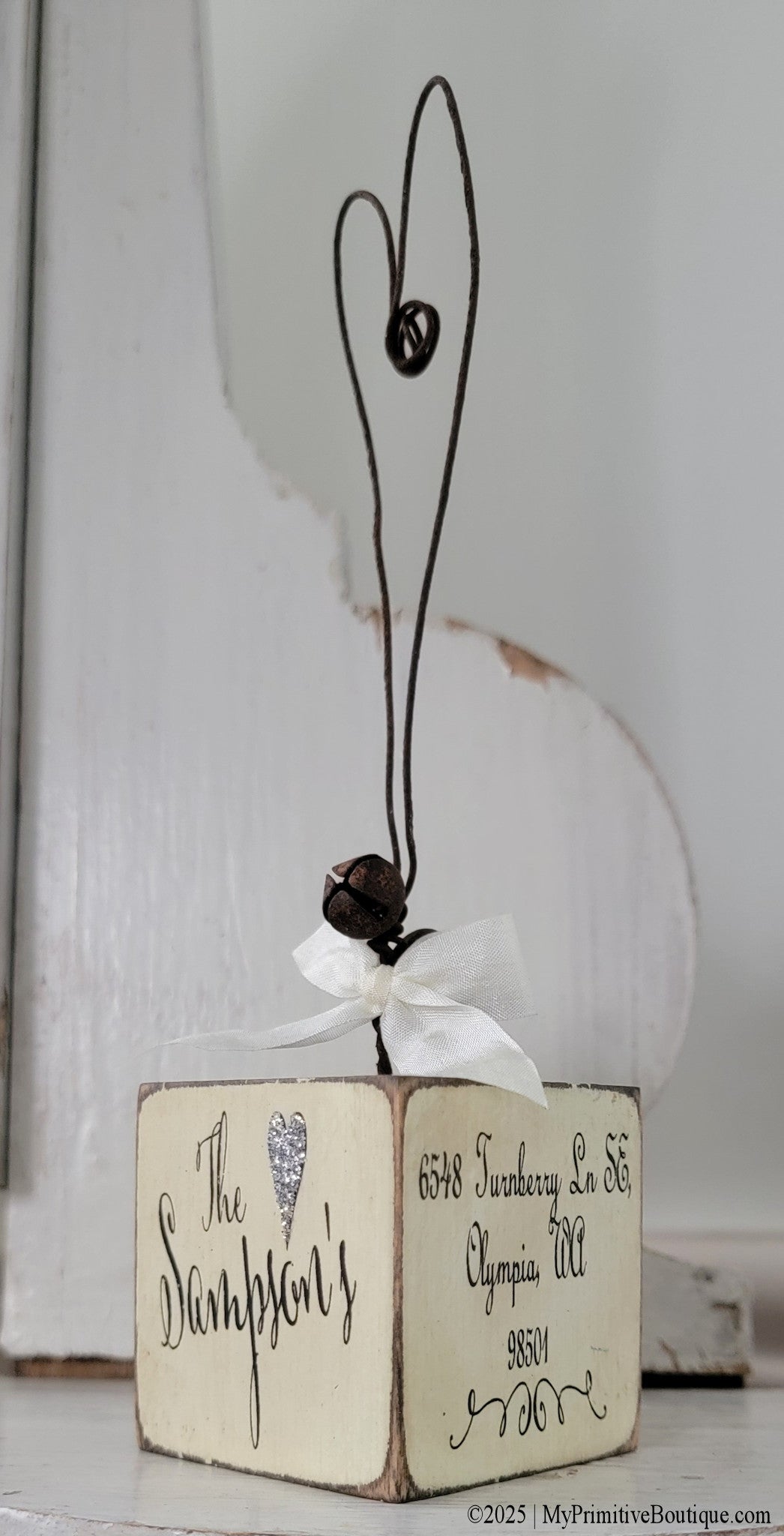 Close-up of distressed ivory hand-painted wooden ornament showing personalized lettering and rustic embellishments.